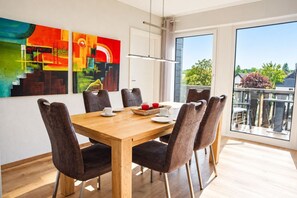 A dining area with a wooden table, six chairs, and a view of the outdoors through large windows. - Siebenstern**** Vacation Rental - 4-star vacation rental with high-speed Wi-Fi, balcony & (Winterberg)