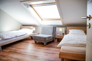 A dormitory room with two single beds, a grey armchair, and a skylight.