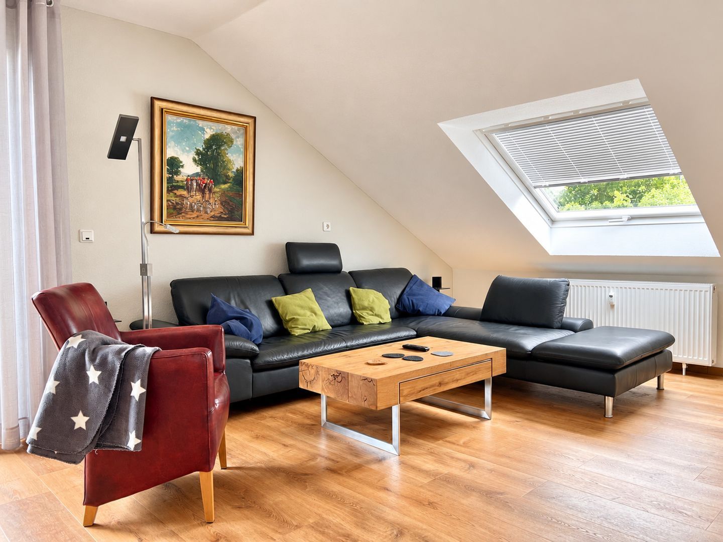 A modern living room with a sloped ceiling, a black leather sofa, a wooden coffee table, and a red armchair.