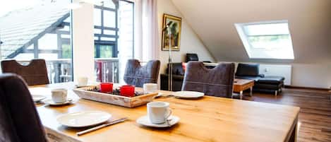 A dining area with a wooden table, chairs, and a tray of food. There are windows and a view of the outside.