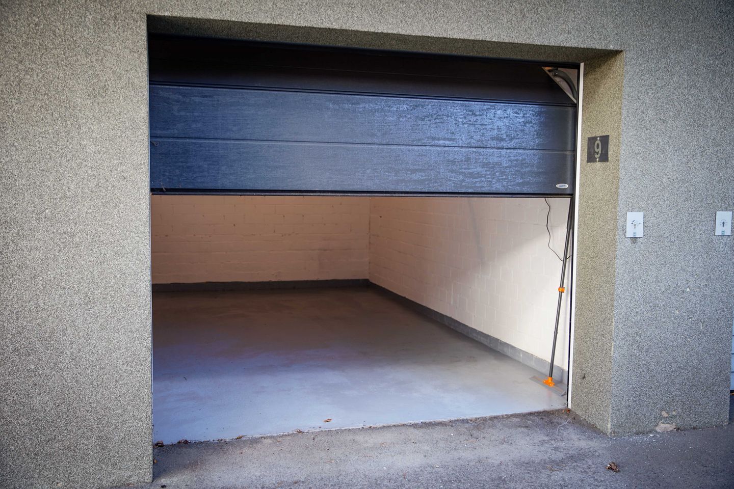 A garage with a closed door, a concrete floor, and a brick wall.