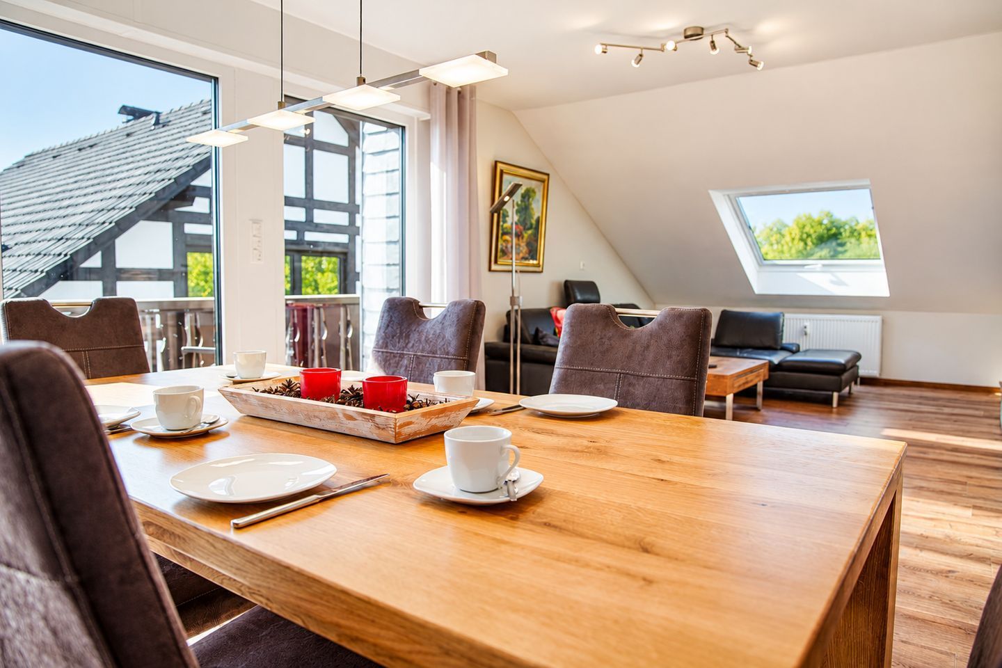 Een eetruimte met een houten tafel voor vier personen, een schilderij aan de muur en uitzicht op het landschap door een raam.