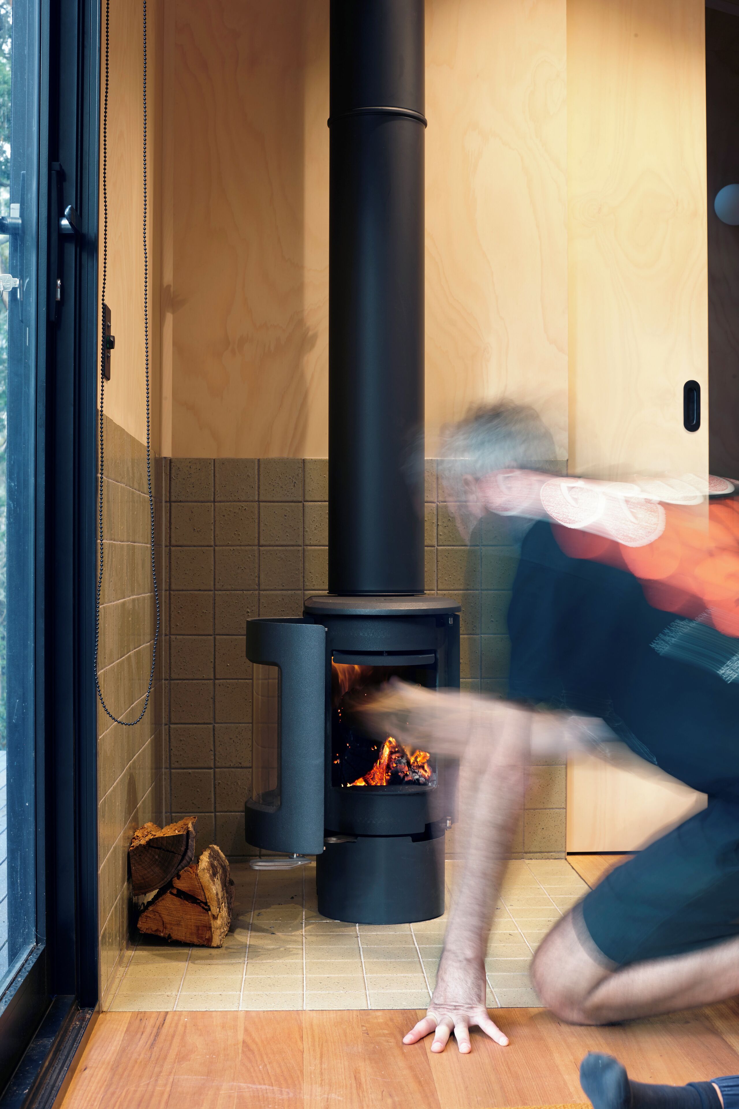 A modern interior with a wood-burning stove, tiled walls, and a wooden floor.