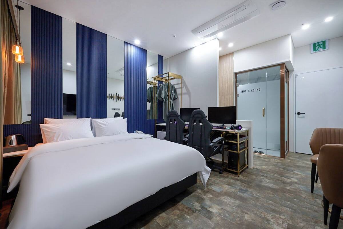 A hotel room with a large bed, a desk with a computer, a chair, and a wardrobe.
