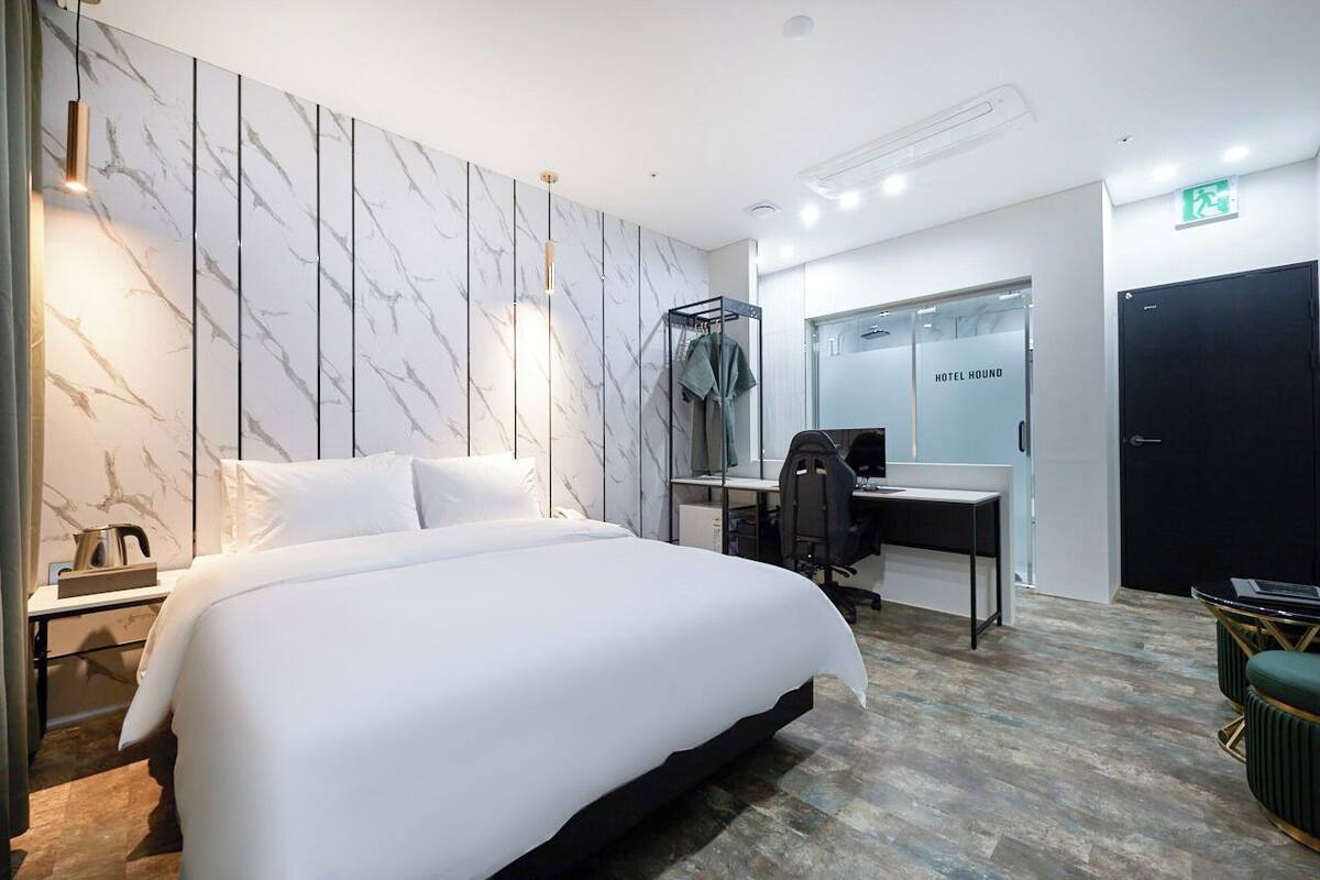 A modern hotel room with a large bed, a desk, and a chair. There is a wardrobe and a mirror on the wall.