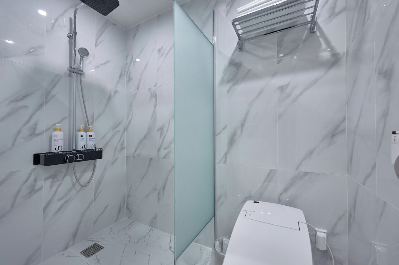 Ein modernes Badezimmer mit einer Duschkabine aus Glas, einem weißen Waschbecken und einer Wand mit Marmorfliesen.