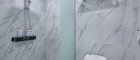 Ein modernes Badezimmer mit einer Duschkabine aus Glas, einem weißen Waschbecken und einer Wand mit Marmorfliesen.