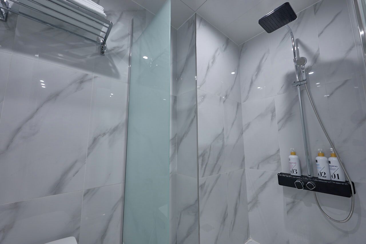 A modern bathroom with a glass shower enclosure, a handheld showerhead, and a shelf with toiletries.