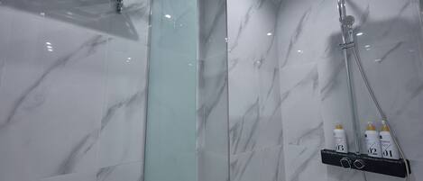 A modern bathroom with a glass shower enclosure, a handheld showerhead, and a shelf with toiletries.