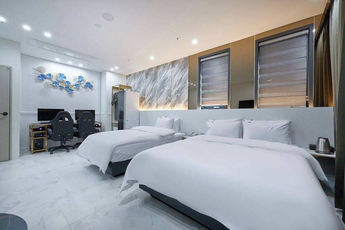 A modern hotel room with two beds, a desk with a computer, and a decorative wall piece.