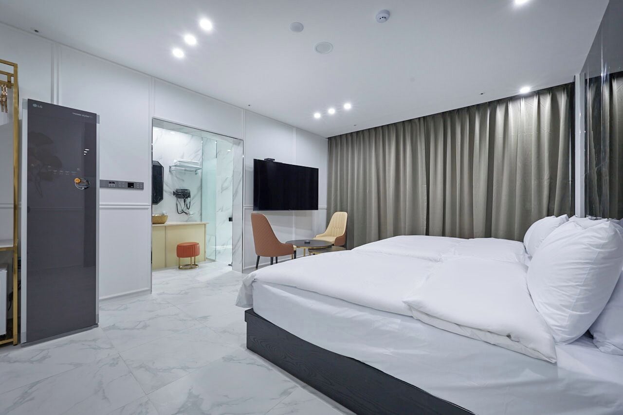 Habitació d'hotel moderna amb un llit gran, una taula de treball, una cadira, un televisor i una dutxa amb envàs de vidre.