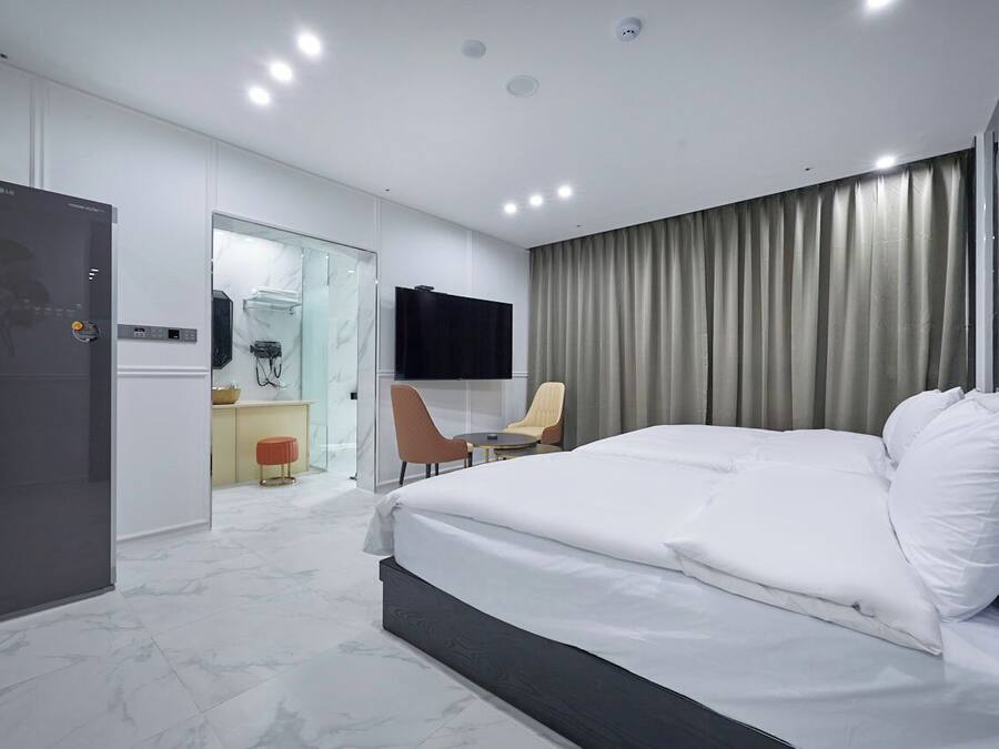 Habitació d'hotel moderna amb un llit gran, una taula de treball, una cadira, un televisor i una dutxa amb envàs de vidre.