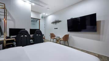 Een hotelkamer met een groot bed, twee stoelen, een bureau met een computer, een aan de muur bevestigde televisie en een bijzettafeltje.