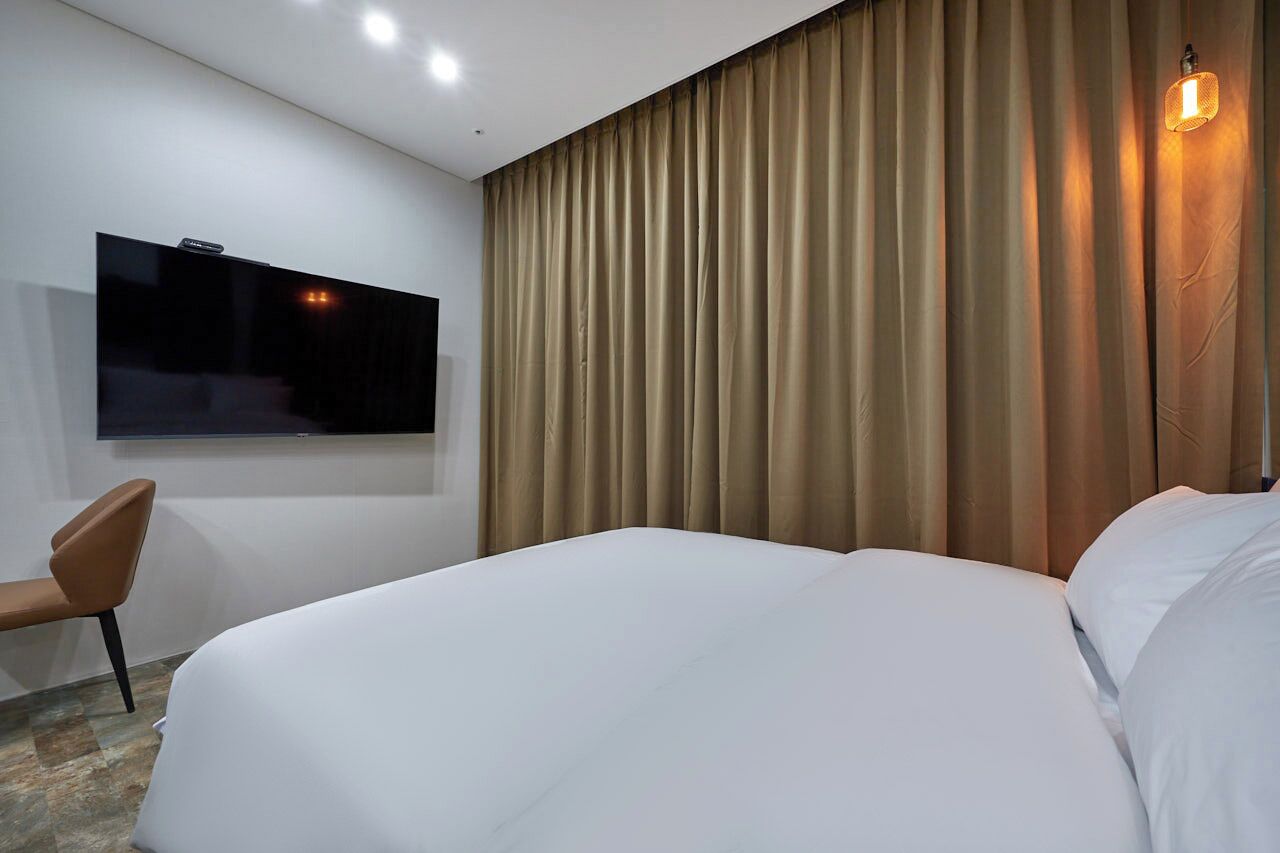 A hotel room with a large bed, a flat-screen TV mounted on the wall, a chair, and a curtain.
