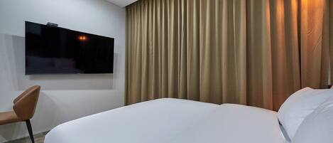 A hotel room with a large bed, a flat-screen TV mounted on the wall, a chair, and a curtain.