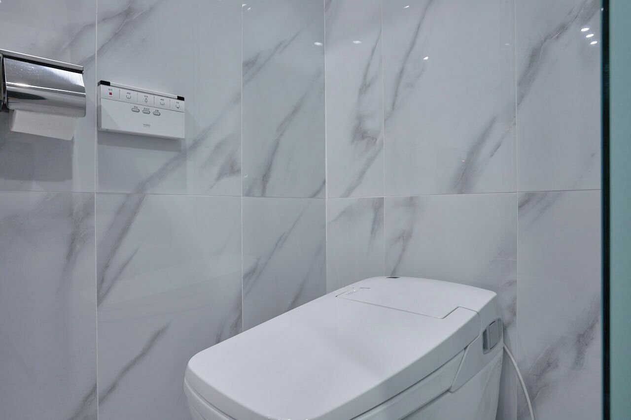 Ein modernes Badezimmer mit Toilette, einem Händetrockner und einer Bedienkonsole an der Wand.