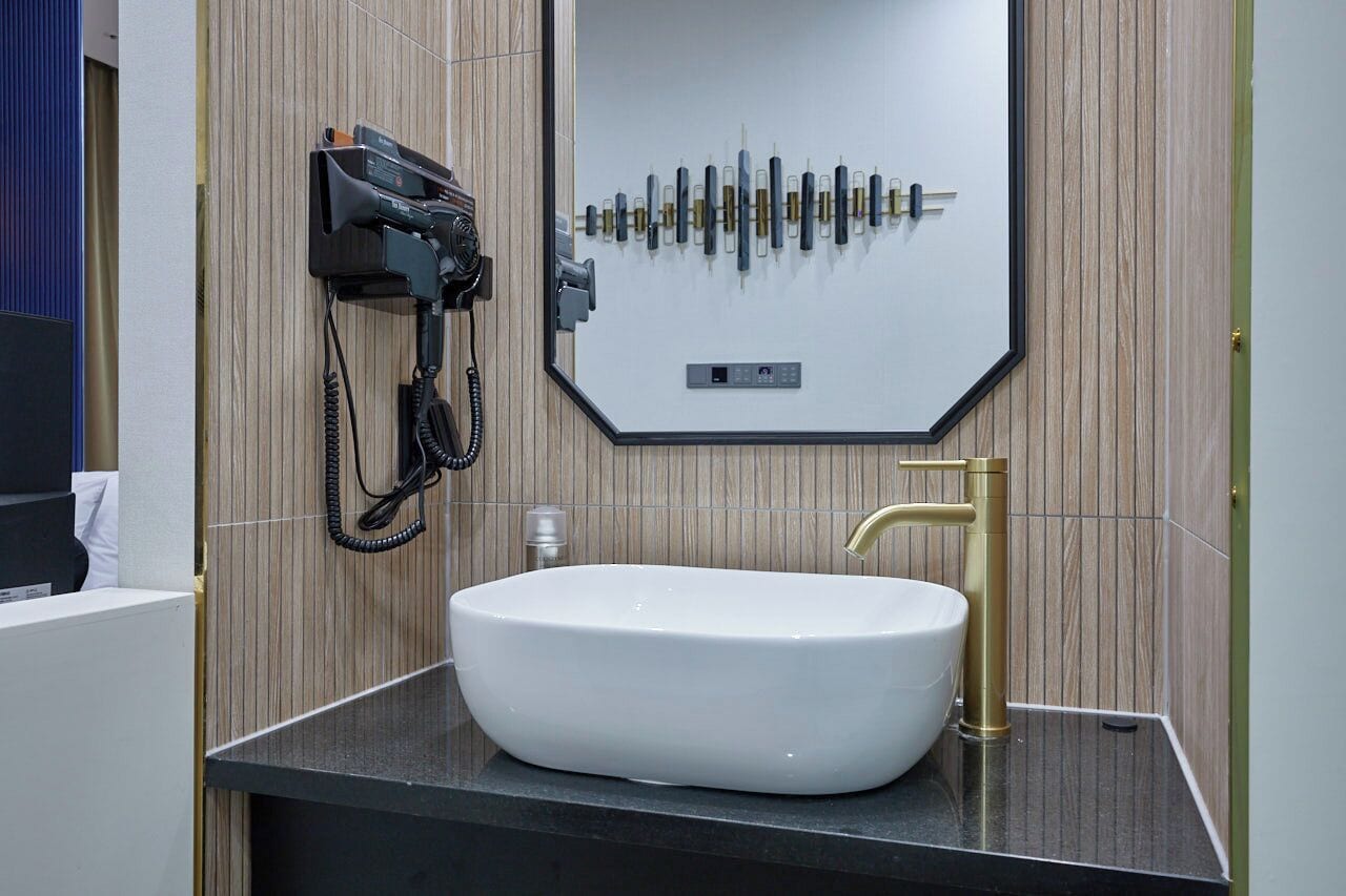 Een badkamer met een witte wasbak, een gouden kraan en een spiegel met een ontwerp van een geluidsgolf.