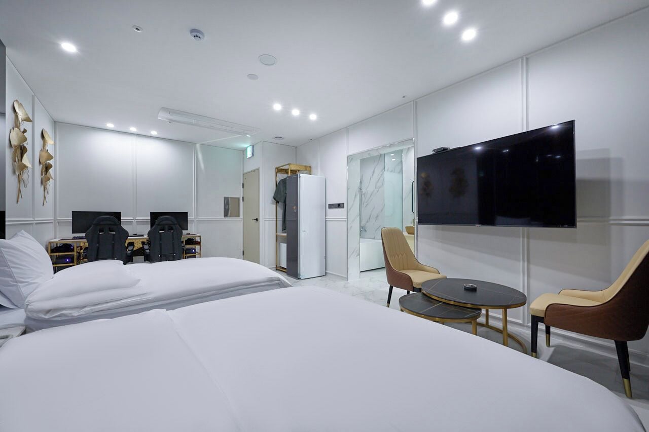 A modern hotel room with a large bed, a TV, a desk with two chairs, and a small table.