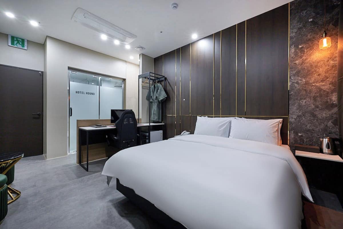 A hotel room with a large bed, a desk with a chair, a wardrobe, and a wall-mounted light fixture.