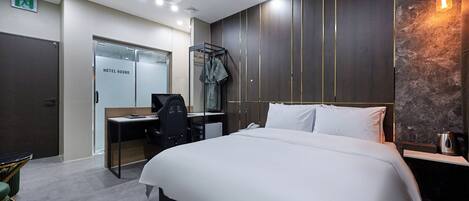 A hotel room with a large bed, a desk with a chair, a wardrobe, and a wall-mounted light fixture.