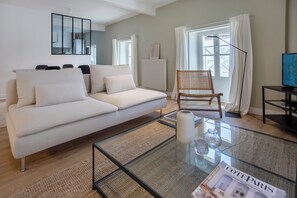 Een moderne woonkamer met een bank, een glazen salontafel en een rieten fauteuil.