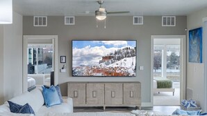 A living room with a large TV, a ceiling fan, and a view of a snowy landscape through the window. - Convention Ctr! Spacious 2BR/2BA-Spa,Pool,Gym,Pkg (Salt Lake City)