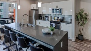 A modern kitchen with a central island, bar stools, stainless steel appliances, and a potted plant. - Convention Ctr! Spacious 2BR/2BA-Spa,Pool,Gym,Pkg (Salt Lake City)