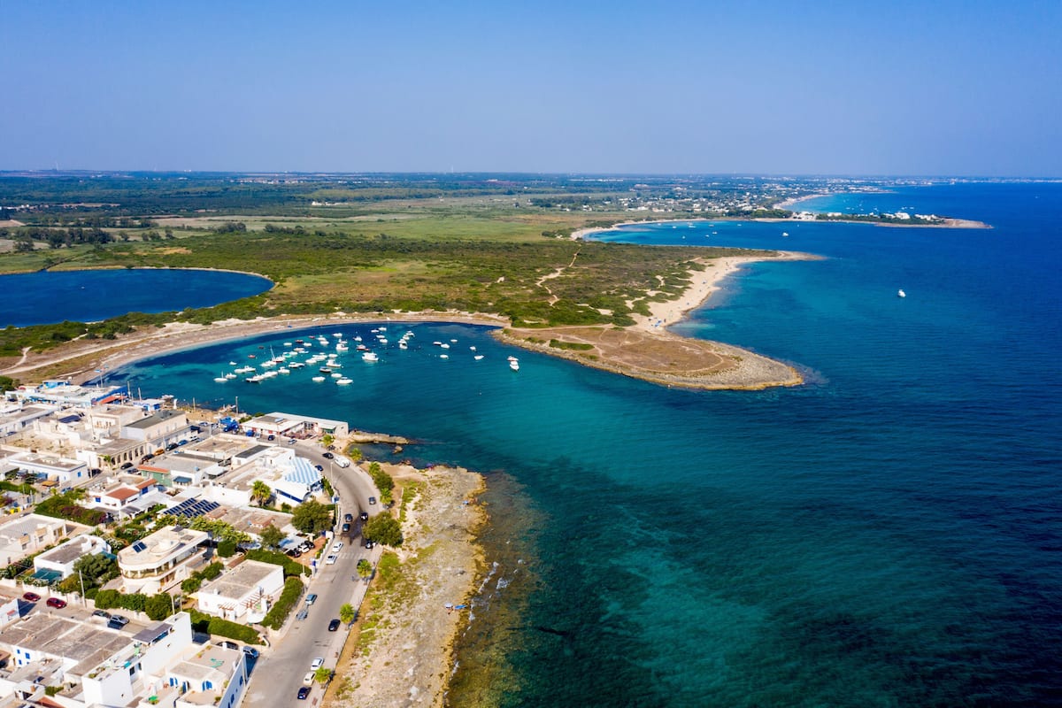 Une vue aérienne d’une ville côtière, avec des eaux d’un bleu limpide, des bateaux et des bâtiments qui bordent la côte.