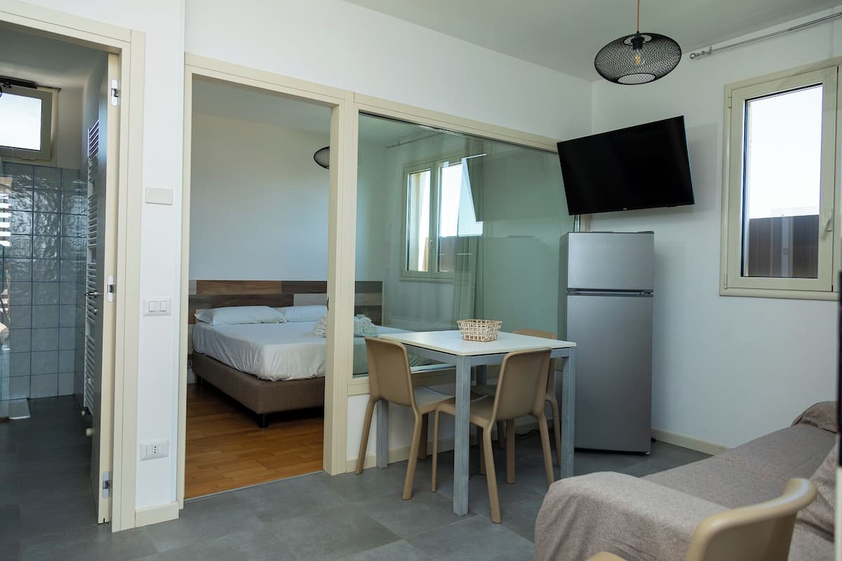 Une chambre d’hôtel de taille réduite, comprenant un lit, une petite table à manger avec des chaises, un réfrigérateur et un téléviseur fixé au mur.