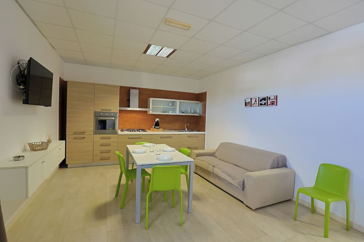 Un espace de vie compact comprenant un coin cuisine, une table à manger avec des chaises, un canapé et un téléviseur fixé au mur.