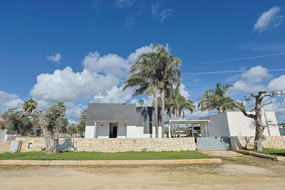 Une maison moderne avec un mur en pierre, un palmier et un ciel d’un bleu éclatant.