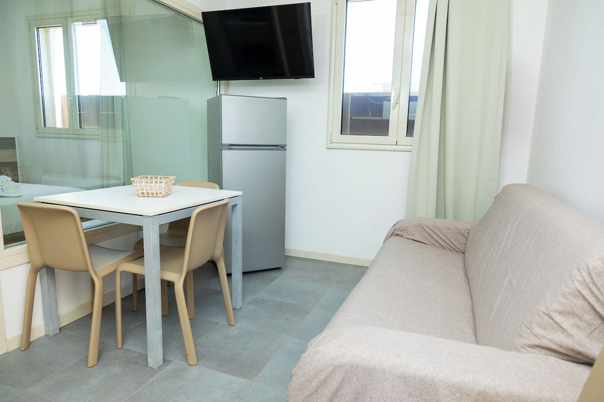 Un espace de vie compact comprenant un coin cuisine, un coin repas avec une table et des chaises, un canapé et un téléviseur fixé au mur.