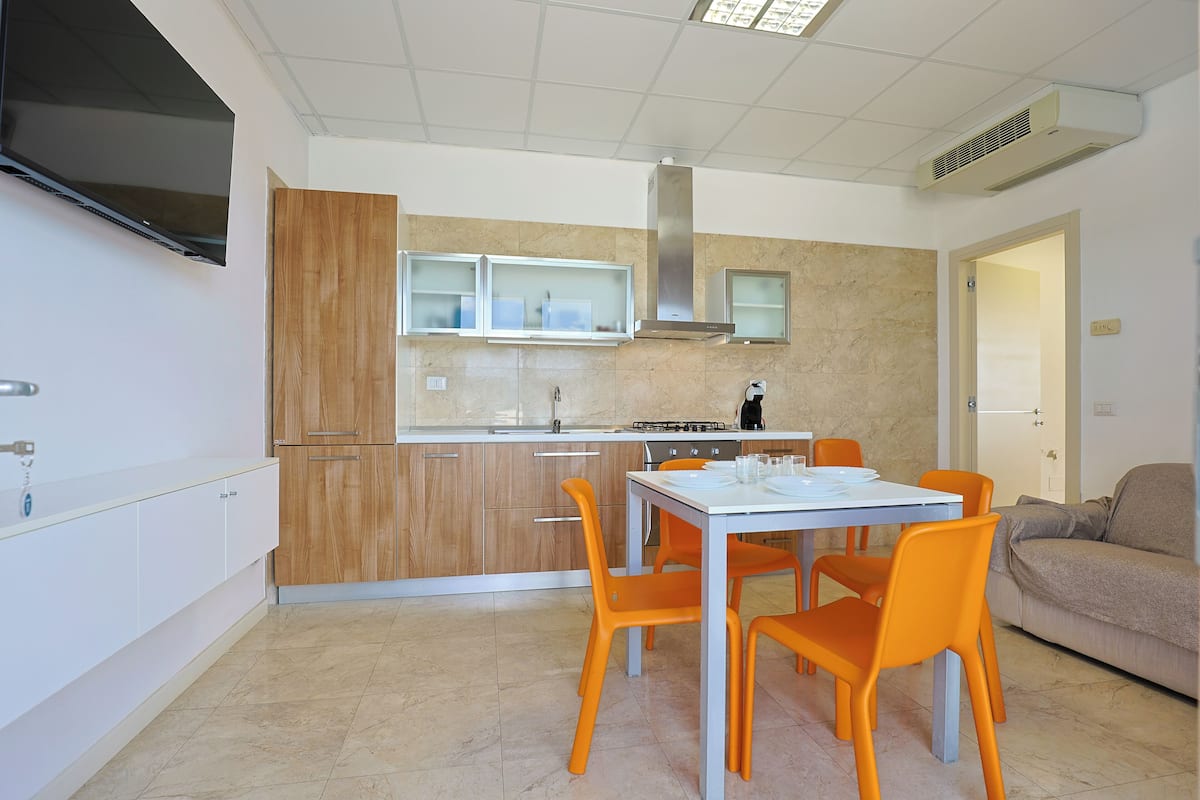 Une cuisine moderne avec des meubles en bois, un plan de travail blanc et un coin repas doté de chaises orange.