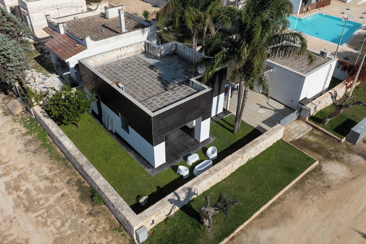 Vue aérienne d’une maison moderne dotée d’un toit plat, d’une piscine et d’une pelouse bien entretenue.