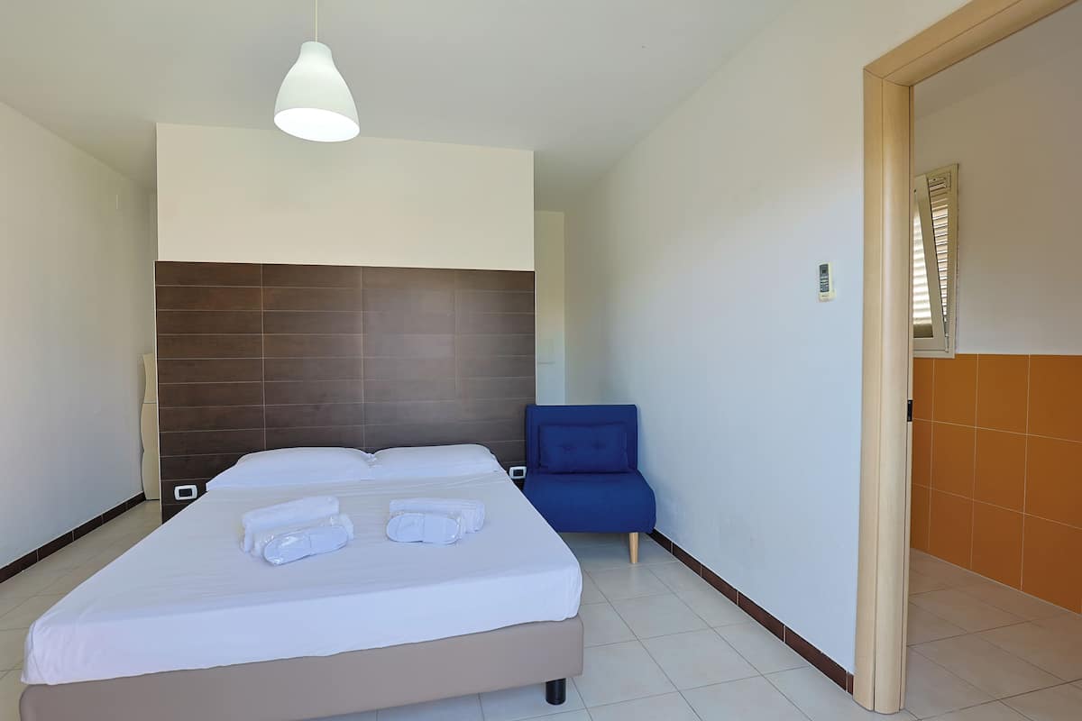 Une chambre d’hôtel avec un grand lit, une chaise bleue et un luminaire moderne.