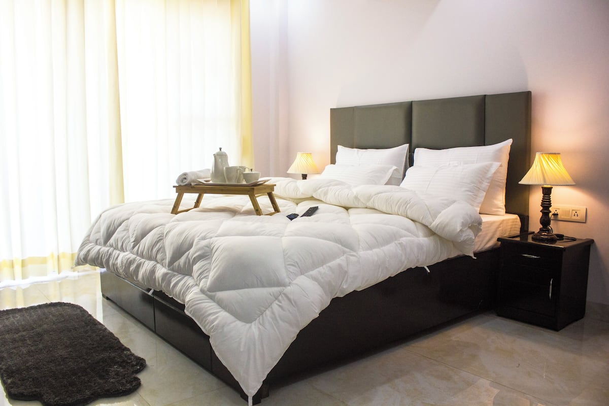 A neatly made bed with a dark headboard, a bedside table with a lamp, and a tray with cups and a teapot.