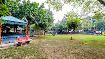 Relax in a serene park setting with a charming gazebo and adjacent bench, surrounded by lush greenery and a family-friendly playground.