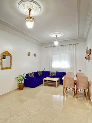 Una sala de estar con un sofá azul, una mesa de centro de madera y un comedor con sillas.