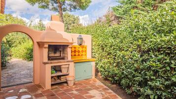 Een buitenkeuken met een stenen vloertegel, een ingebouwde oven en een groen kastje.