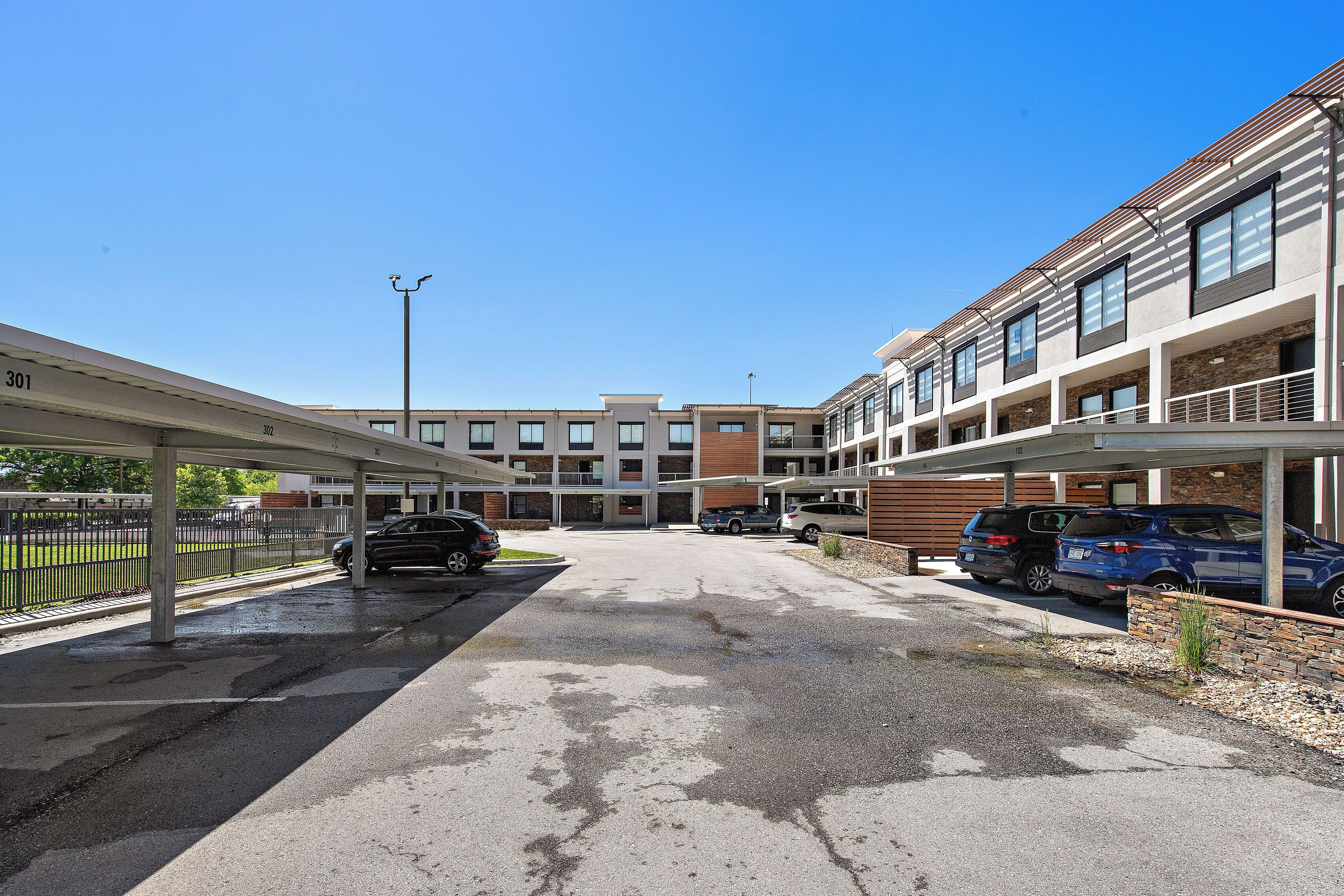 A parking area with cars, a covered walkway, and a building with multiple floors and windows.