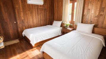 Een kamer met twee bedden, houten wanden, een raam met gordijnen, een nachtkastje met een vaas en een deur met deurmat.