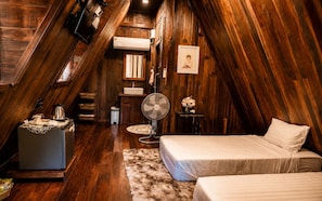 A cozy attic bedroom with wooden walls, a bed, a small table, a fan, and a kitchenette. - Punnattha House by Peema Villa (U Thong)