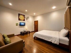 A bedroom with a bed, a wooden floor, a TV, a fan, and a door. - Punnattha House by Peema Villa (U Thong)