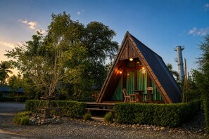 Una cabaña de madera triangular con una cortina verde, dos sillas y una mesa al frente.
