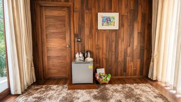 A room with a wooden door, a small refrigerator, a basket of snacks, and a framed picture on the wall.