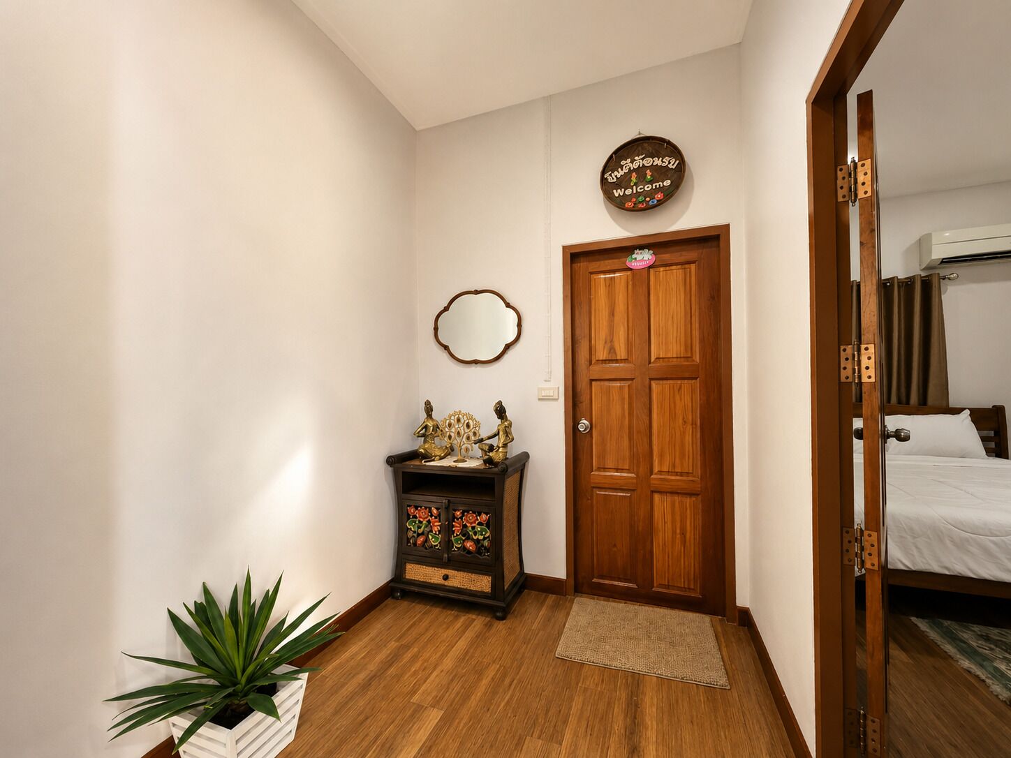 Una habitación con puerta de madera, un mueble pequeño con objetos decorativos, un espejo y una planta en maceta.