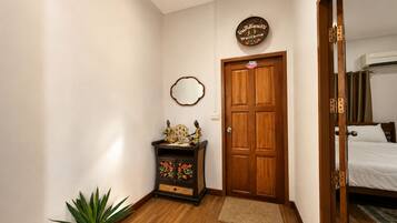 Una habitación con puerta de madera, un mueble pequeño con objetos decorativos, un espejo y una planta en maceta.