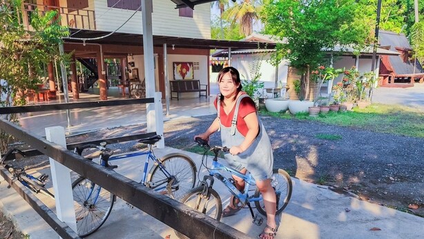 A person riding a bicycle on a concrete path with a metal railing. - Punnattha House by Peema Villa (U Thong)