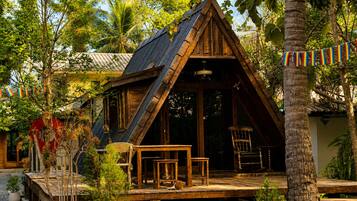 A wooden cabin with a sloped roof, a deck with seating, and a view of surrounding greenery.