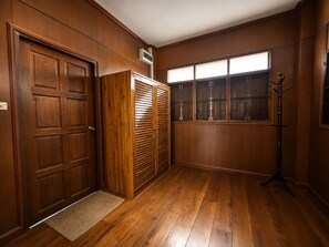 A room with wooden paneling, a large window with blinds, a coat rack, and a door. - Punnattha House by Peema Villa (U Thong)
